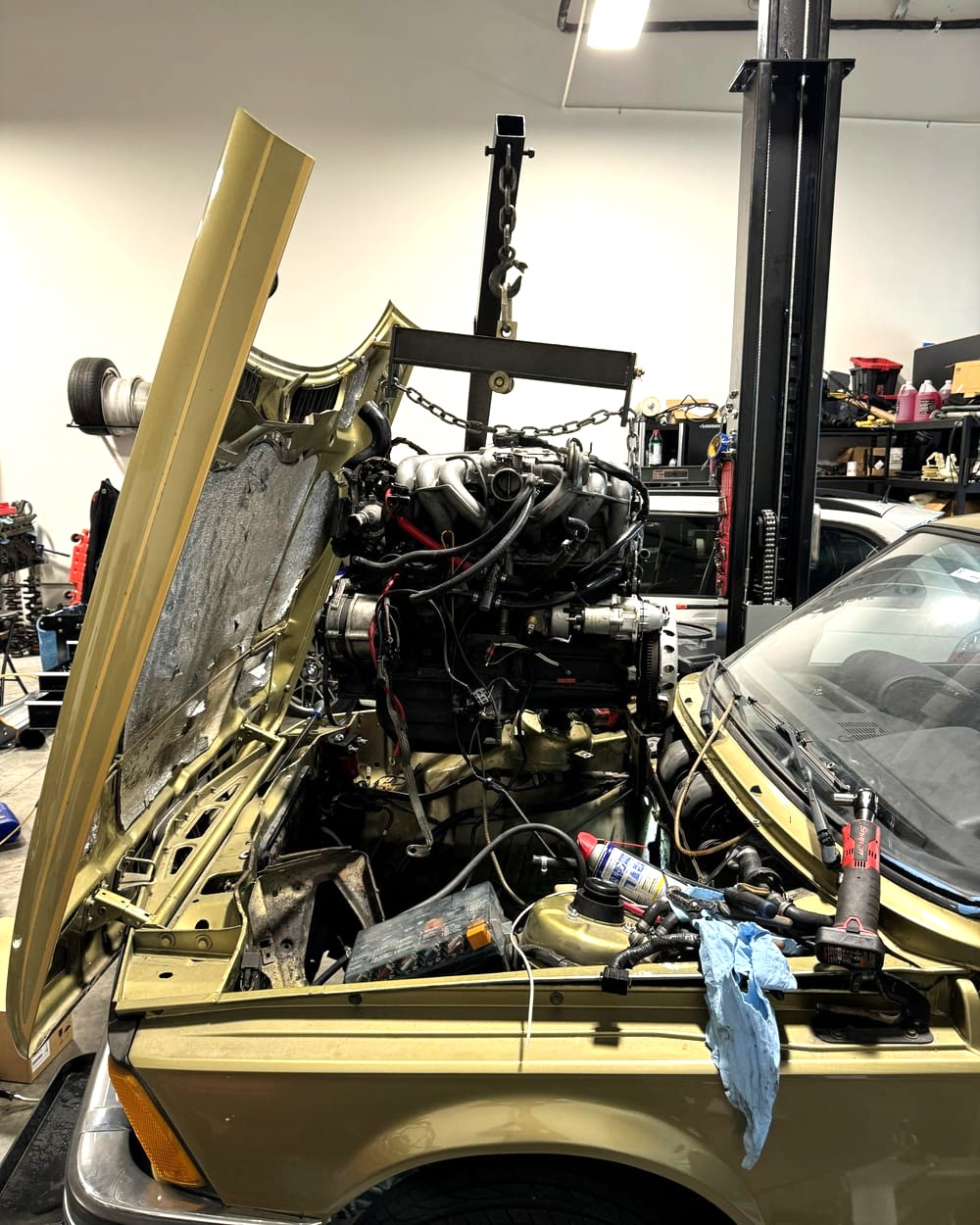 An inline-six on the hoist above a gold BMW in the shop